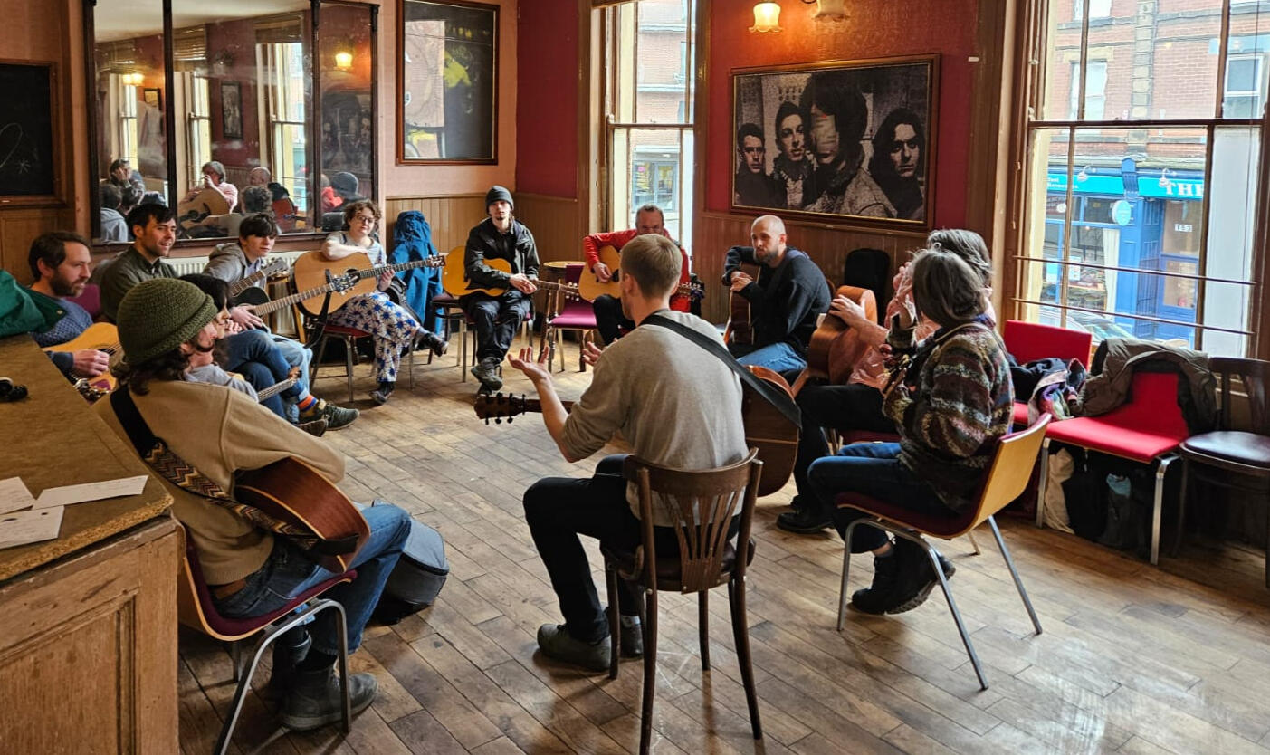 A photo of ten guitarists sat in a circle. Credit: Rhi Good